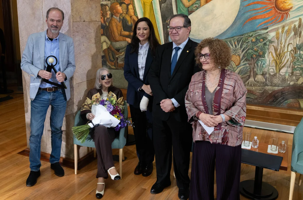 Juan Villoro sostiene el Premio Carlos Fuentes 2026 y posa junto a cuatro asistentes durante la ceremonia en el Palacio de Bellas Artes.