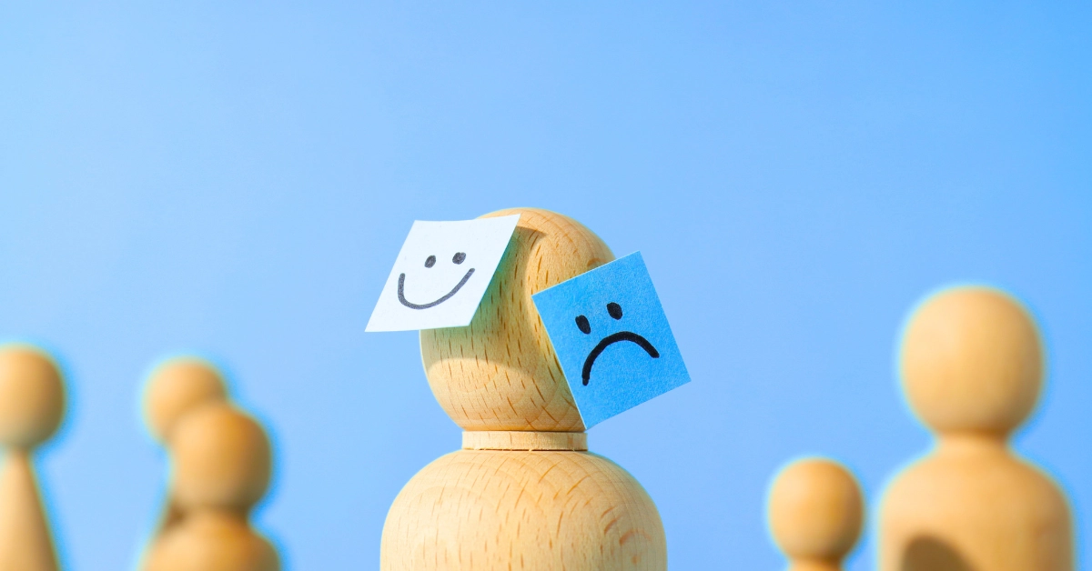 Figura de madera con rostros feliz y triste como representación de la carga mental y las emociones en el entorno laboral.
