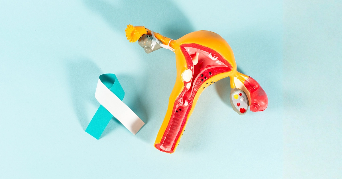 Ilustración anatómica del aparato reproductor femenino junto a un lazo turquesa y blanco, símbolo de concientización sobre el cáncer cervicouterino.
