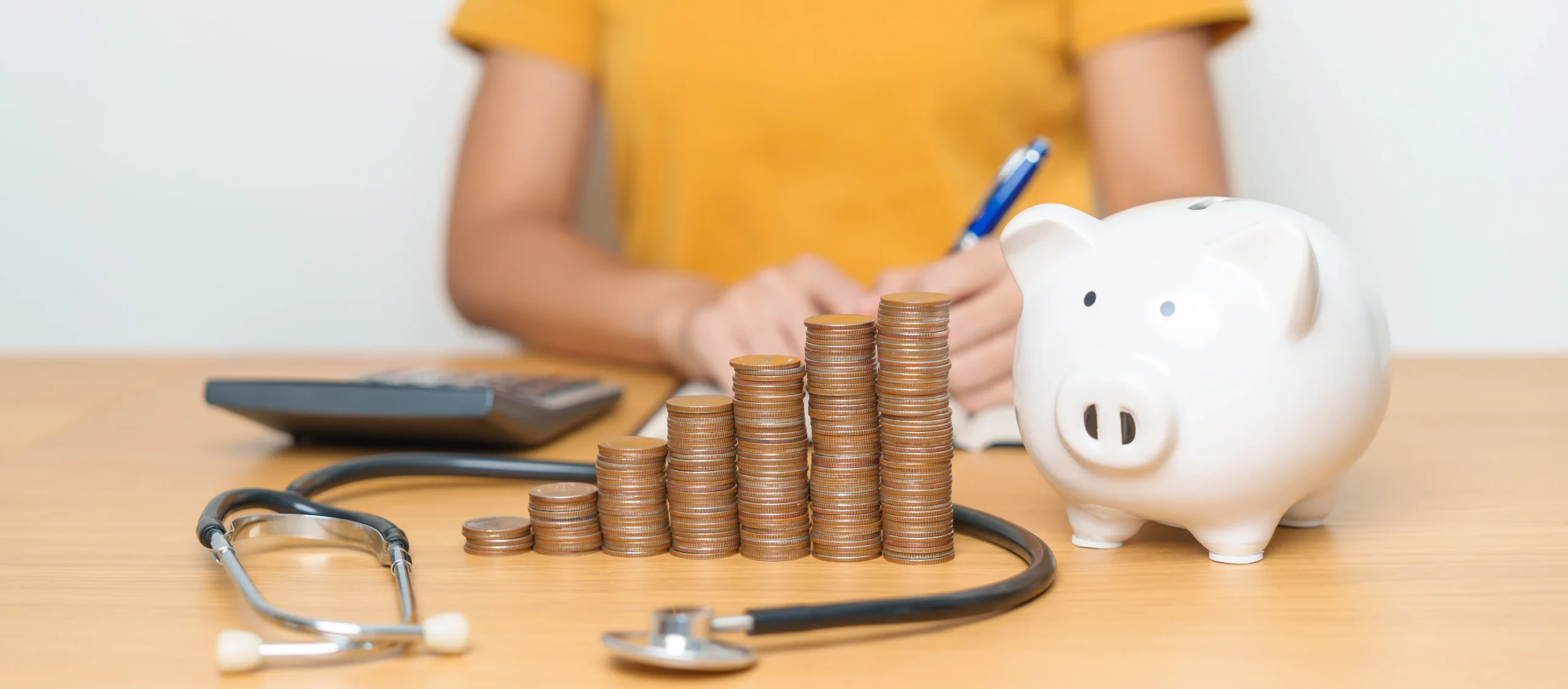 Alcancía y pilas de monedas junto a un estetoscopio como representación del bienestar financiero.